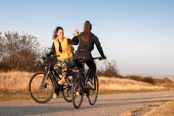 Fototapeta premium Young and happy best female friends in sportswear riding mountain bikes together in nature