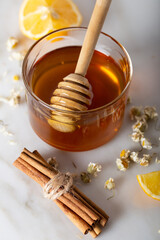 Glass jar full of honey and dipper with dried camomile herb tea, lemon and cinnamon sticks. Herbal supplements concept. 