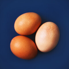 Top view of three brown chicken eggs lying on a blue background. Healthy food for breakfast. Source of protein.
