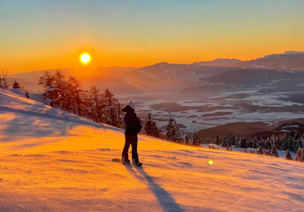LENS FLARE: Female snowboarder observes the golden lit valley before her descent