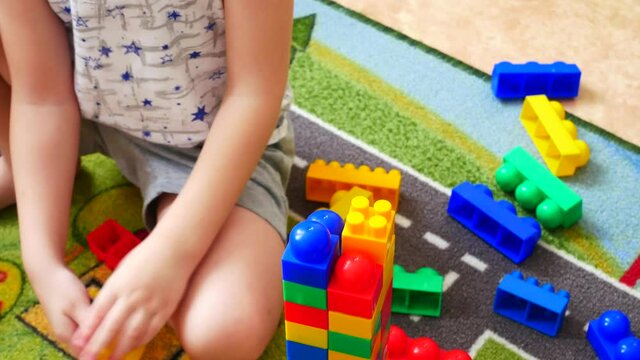 Close-up of a little boy building a tower using colorful constructor blocks sitting on the carpet