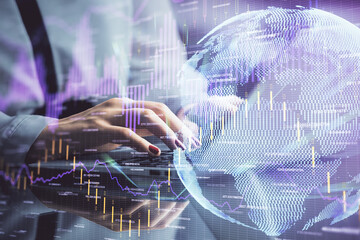 Double exposure of businesswoman hands typing on computer and financial graph hologram drawing....