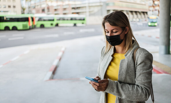 Caucasian young woman with smartphone waiting at bus station while wearing safety mask for coronavirus outbreak - Focus on girl's eye