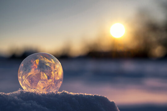 Vereiste Seifenblase auf Schnee mit Sonne im Hintergrund