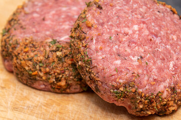 Two fresh raw lamb burgers on wooden chopping board.