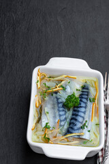 Mackerels in white wine sauce on black stone background