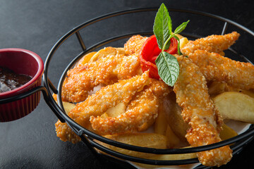 Fried chicken in a metal basket on black background