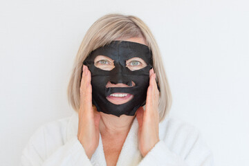 Senior woman applies black cosmetic mask to her face. Anti age concept. Mature woman face after spa treatment. Beauty spa treatment. Plastic surgery clinic, cosmetology, new senior