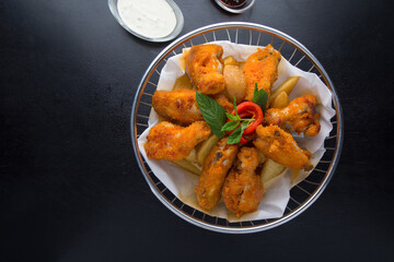Fried chicken in a metal basket on black background