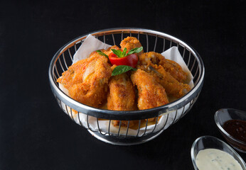 Fried chicken in a metal basket on black background
