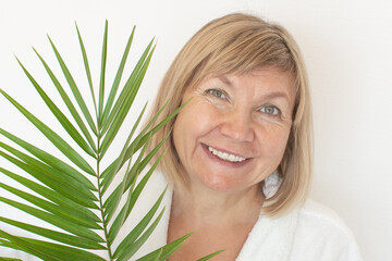 Naklejka premium Senior woman smiling Anti-aging concept with palm leaf. Mature woma face after spa treatment. Old age in joy, plastic surgery clinic, cutie grandmother, cosmetology, new senior