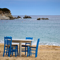 Table with traditional blue chairs at a sandy beach on Sythonia Peninsula, Greece