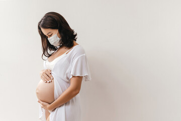 Young beautiful pregnant woman in medical surgical mask at home. Coronavirus, virus, isolation, stay at home.