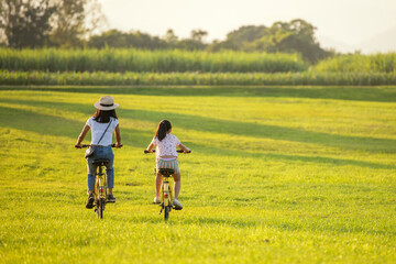 Family Happy.  Mother and daughter smiling happy outdoor with bicycling at the garden meadow in sunset.  Lifestyle Family Concept
