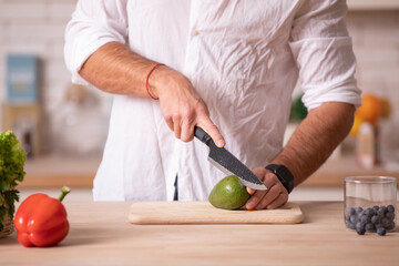 Chef's hands cutting avocado with the help of knife on a white surface