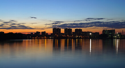 Fototapeta premium River surface in the city at sunset. Reflection of the city lights in the water. Blue sky and water.
