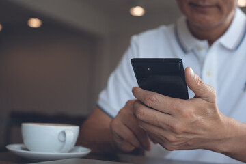 Man in casual wear using mobile phone in coffee shop with cup of coffee on wooden table