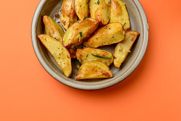 Baked potato with rosemary served in a ceramic bowl over orange background. Delicious idea for dinner.