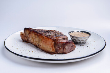 Delicious beef steak with sauce served on a white plate over white background. BBQ meat, barbecue concept.