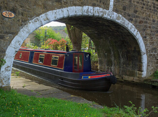 A leisurely boat emerges under the bridge of the Leeds and Liverpool canal at Dowley Gap near Bingley in West Yorkshire