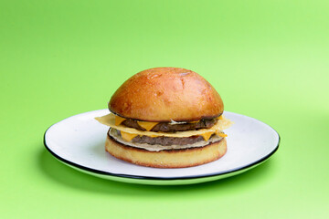 Giant perfect burger with ham and cheese served on a clear white plate over bright green background.