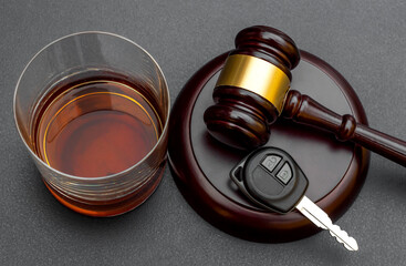 Judge's gavel with car key and glass of whiskey on black.