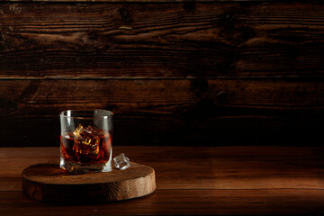 Whiskey with ice or brandy or rum in glass on rustic background. Whiskey with ice in a glass. Whiskey or brandy. Selective focus. Rum with ice on wooden background.