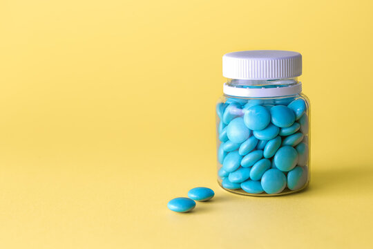 Medication bottle and blue pills on yellow background.