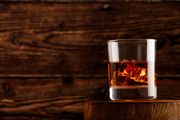 Whiskey with ice or brandy or rum in glass on rustic background. Whiskey with ice in a glass. Whiskey or brandy. Selective focus. Rum with ice on wooden background.