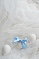 Composition of white easter eggs with bow on the light-blue satin ribbon on white textured background, copyspace