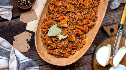 buckwheat porridge with meat and vegetables in wooden oval bowl on rustic table