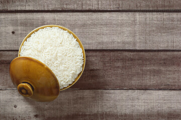 Uncooked dry Thai jasmine rice in bowl isolated on wood floor background, flat lay and top down horizontal view.