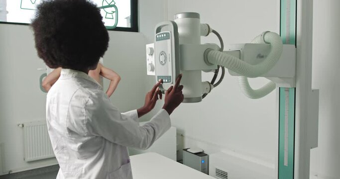 In the Hospital, Man Standing Face Against the Wall While Medical Technician Adjusts X-Ray Machine For Scanning. Scanning for Fractures, Broken Limbs, Chest, Cancer or Tumor.