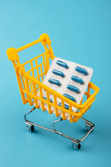Shopping cart loaded with pills drugs or medicine capsules on yellow background.antibiotics. Women's health, medicine and healthcare concept. Top view, copy space for text.