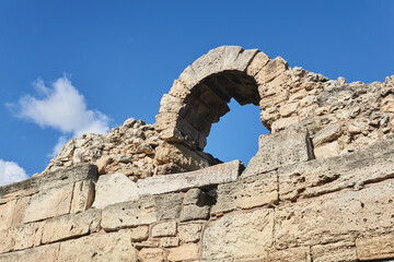 fragment of a destroyed antique fortress wall with arch against the sky