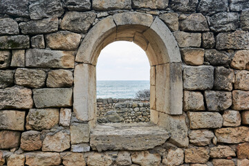 window opening in the ruins of an antique wall, behind which you can see the sea