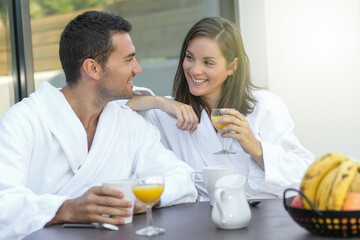 Happy young couple in bathrobes having breakfast outdoors