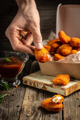 Close-up of the hands holding home made tasty Chicken nuggets and sauce in paper box on a wooden background. American food concept. fast food meal. banner, menu, recipe, place for text