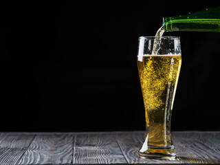 Pouring beer from a bottle into a glass glass on a dark background on a wooden table