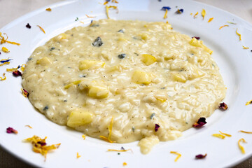 Risotto all’onda servito nel piatto di ceramica guarnito con petali di fiori commestibili