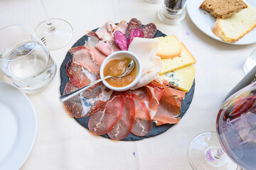 Piatto con misto di salumi affettati e fette di formaggio serviti con una salsina nella ciotolina bianca 