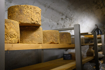 Forme rotonde di formaggio stagionato sul ripiano in legno dello scaffale nel magazzino di stagionatura