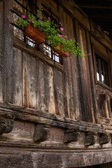 Fototapeta na wymiar Particolare di una tipica antica costruzione in legno con finestre abbellite da vasi con fiori
