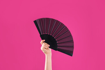 Woman holding black hand fan on pink background, closeup - obrazy, fototapety, plakaty