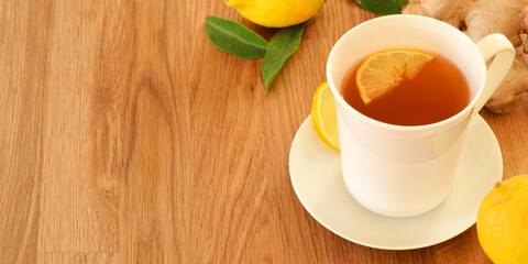 Hot tea with fresh lemon fruit and ginger in white porcelain cup on wooden table. Healthy treatment of cold and flu disease.