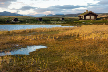 Golden hour in mountain scenery with cabins and lake and dramatic skies.