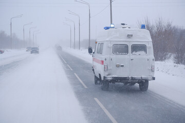 Heavy snowfall and blizzard. An ambulance goes to help on the road. Part of the image is blurred.