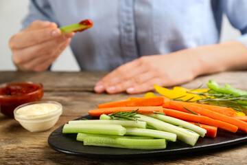 Plate with celery sticks, other vegetables and different dip sauces on wooden table, closeup