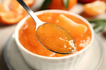 Spoon with delicious tangerine over bowl, closeup