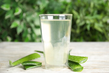 Fresh aloe drink in glass and leaves on white wooden table